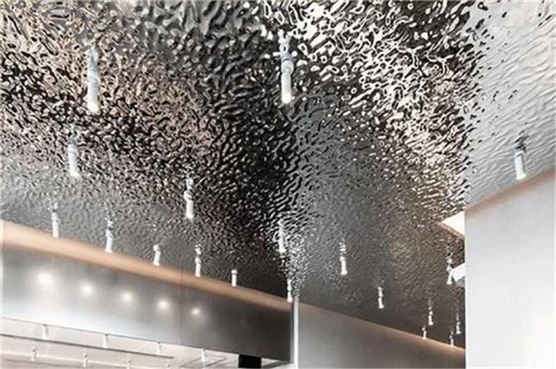 A reflective metal ceiling with a repeated raised texture and rows of recessed lights is shown in a finished interior.